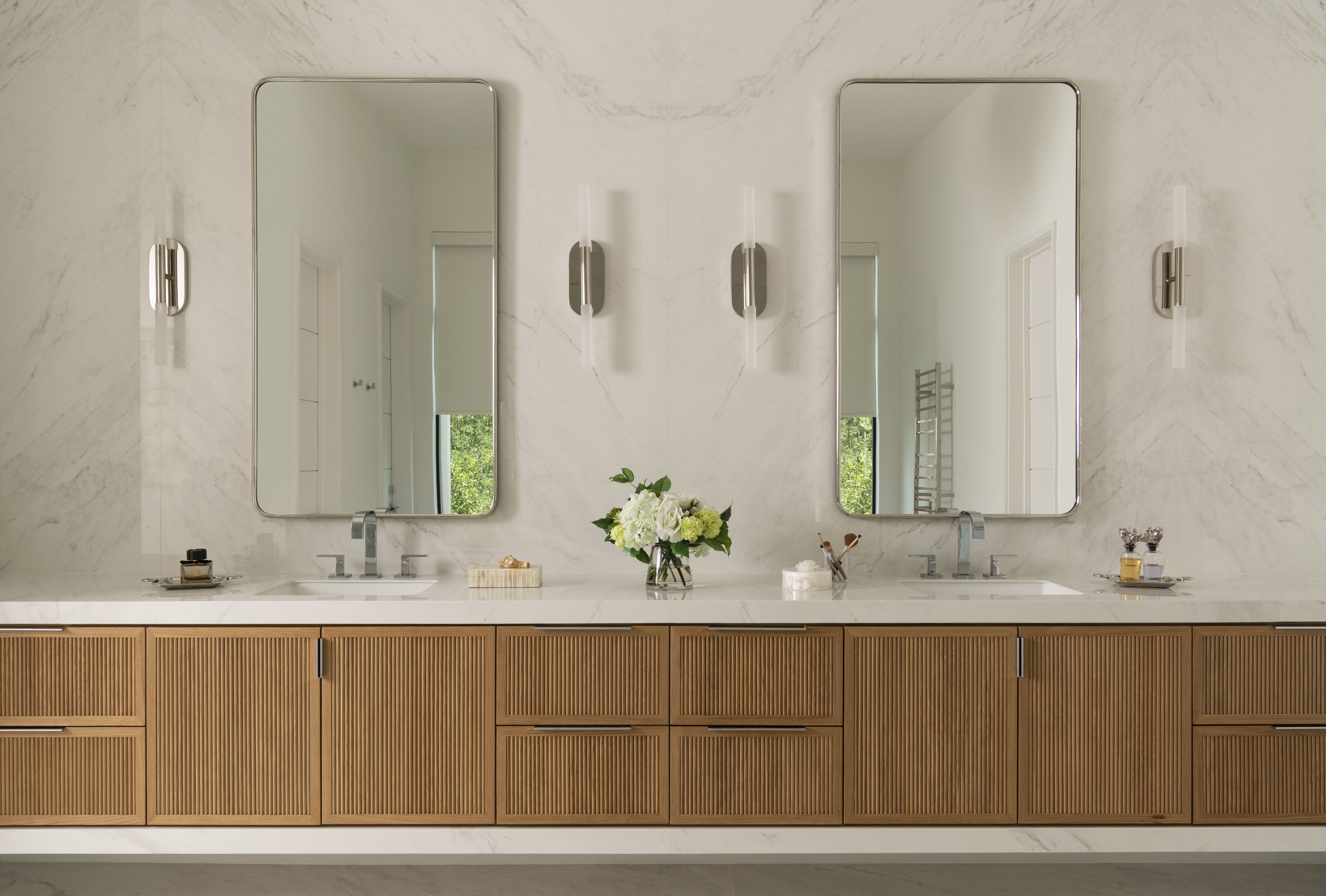Spa-like bathroom with dual mirrors, marble surfaces, wood-paneled cabinetry, and soft natural lighting.