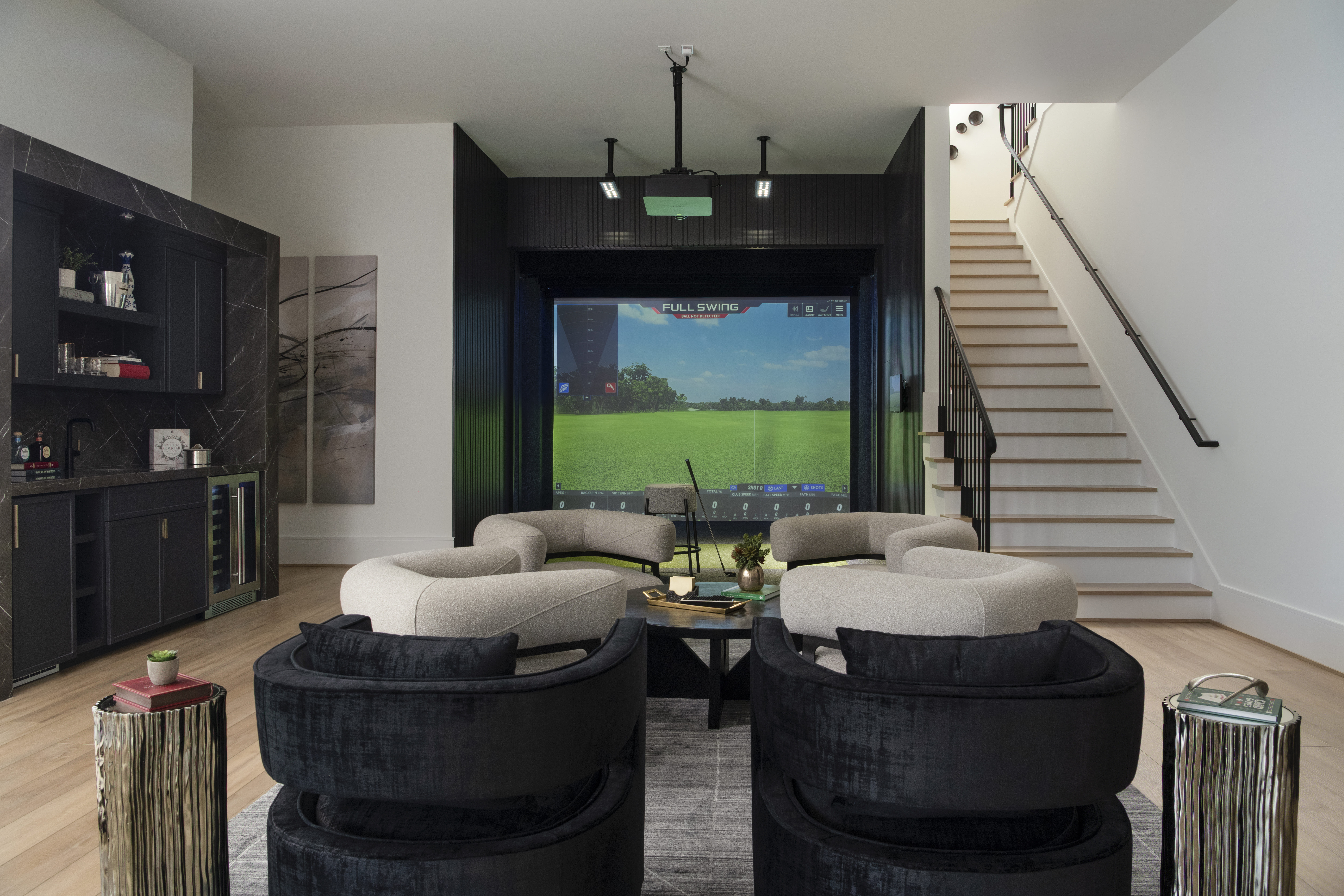 Entertainment room with curved lounge seating, a golf simulator screen, and a built-in bar with dark cabinetry.